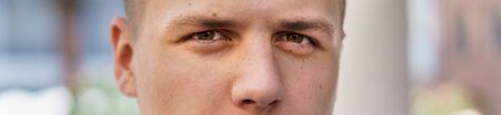Panorama banner in a close up cropped view of the eyes of a young man looking intently at the camera...