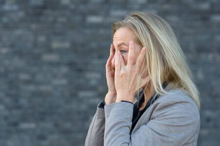 Shocked blond woman with her hands to her cheeks, looking up and screaming. Close-up side portrait...
