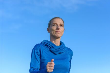 Thoughtful attractive middle aged woman jogging outdoors standing staring ahead with a faraway...