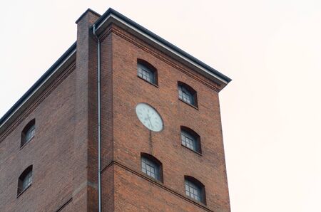 Exterior of a commercial red brick building or industrial factory with clock on the wall viewed low angleの写真素材