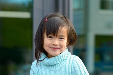 Fun happy pretty little girl grinning at the camera as she poses outdoors in front of a building...