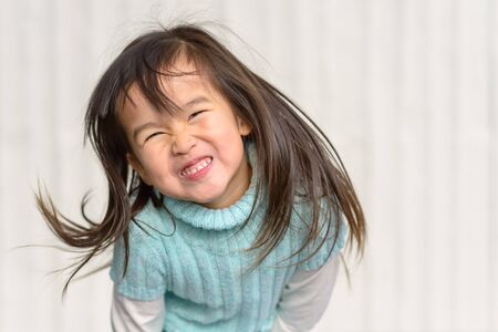 Fun loving little girl tossing her long hair as she grins at the camera over a white textured...
