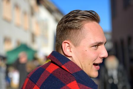 Young man turning to look over his shoulder as he speaks with mouth open outdoors in evening light in an urban squareの写真素材