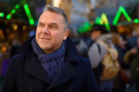 Serious stylish middle-aged man in winter outfit standing in an urban square and looking upの写真素材
