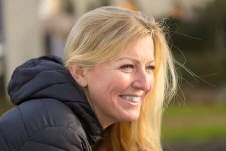 Profile headshot of a pretty young blond woman with a happy smile in an urban environment