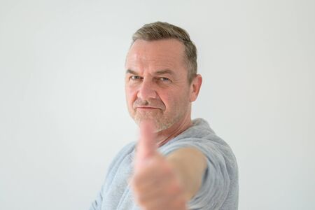 Middle-aged man outstretches his hand with thumb up gesture, blurred in selective focus in foreground. Close-up front portrait against grey backgroundの写真素材