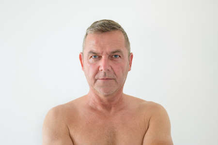Serious middle-aged man posing shirtless staring intently at the camera with a serious expression in a head and shoulders portrait on a white backgroundの写真素材