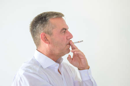 Thoughtful middle-aged man smoking a cigarette looking to the side as he takes a long puff over a...