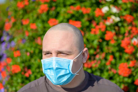 Young man wearing a surgical face mask during the Covid-19 or coronavirus pandemic outdoors against...