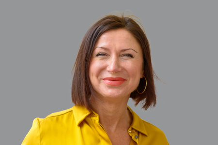 Attractive middle aged brunette woman with a lovely big warm friendly smile in front of an grey...