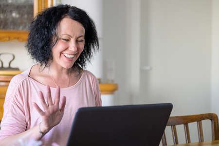 Woman waving with her hand to the computer while doing home office during the  pandemic lockdown