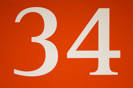 Colorful red and white sign with the number thirty-four - 34 - stencilled in the centre in a full...