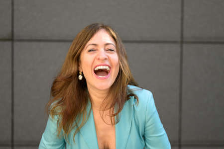 Happy fun loving attractive middle-aged woman laughing at the camera in a head and shoulders portrait against a grey wallの写真素材