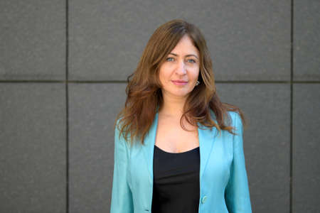 Attractive blue-eyed woman looking at the camera with a quiet smile as she poses in front of a tiled wall on a commercial buildingの写真素材