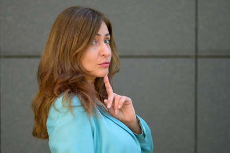 Sceptical woman looking sideways at the camera with a knowing expression and finger to her chin in a...