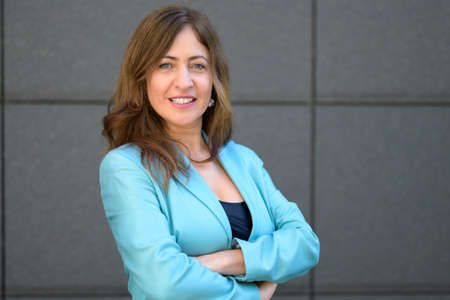 Confident smart middle-aged businesswoman with folded arms turning to stare intently at the camera...