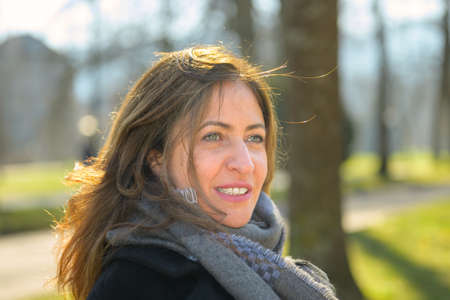 Attractive woman sitting daydreaming on a bench in a park in early spring in a close up oblique head...