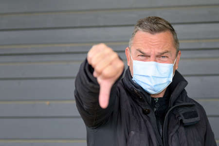 Portrait of a middle-aged man wearing protection mask while showing a thumb down sign with both handsの写真素材