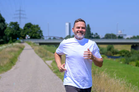Close up of a fit active healthy senior man jogging along a footpath approaching the camera with a happy smileの写真素材