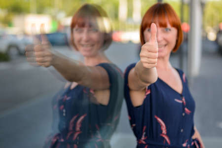 Excited surprised redhead woman giving a thumbs up gesture with a look of amazement with focus to her fingerの写真素材