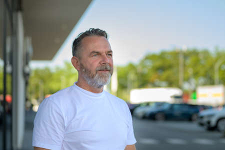 Thoughtful bearded senior man standing in an outdoor carpark looking aside with a quiet pensive expression in a head and shoulders portraitの写真素材