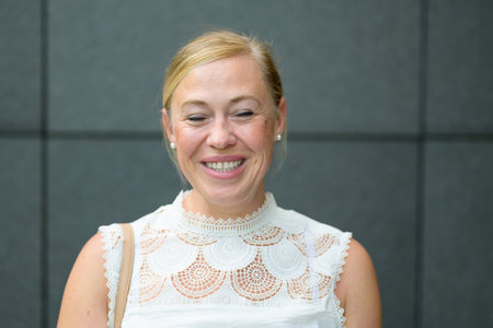 Candid headshot portrait of a happy beaming blond middle-aged woman with closed eyes posing against...