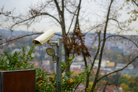 Old weathered surveillance camera and solar light in shrubbery overlooking a city below in a close up view with partial signboardの写真素材
