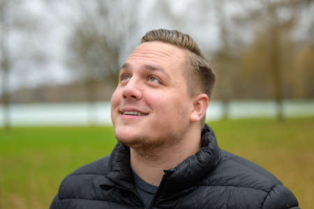 Intrigued young man looking up with a smile outdoors in a park in a head and shoulders portrait