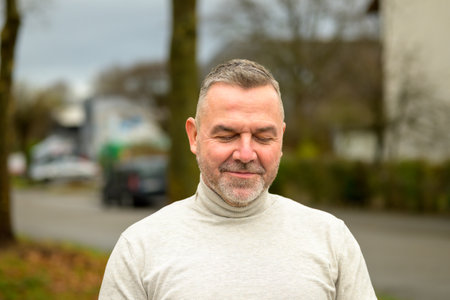 Man standing relaxing with closed eyes and a contented smile in an urban street in a head and...