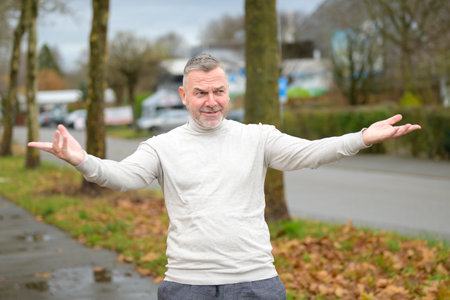 Senior man making an expansive gesture with his arms stretching them wide with a quiet smile...