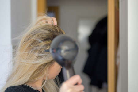 Woman drying her long blond hair with a hairdryer after washing it in a closeup side viewの写真素材