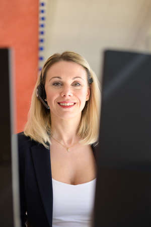 Smiling young female call centre executive using a headset and computer in a modern officeの写真素材
