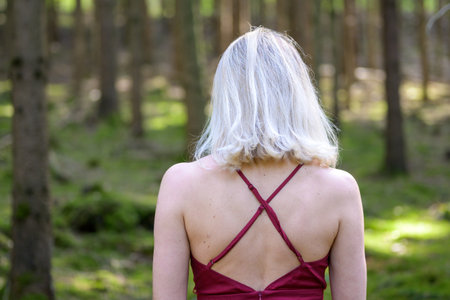Rear view of woman with medium-length blond hair wearing backless magenta dress in forestの写真素材
