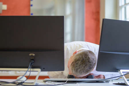 Businessman sitting slumped over his desk in an office after suffering a heart attackの写真素材