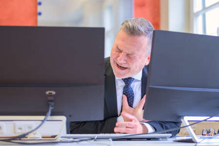 Businessman suffering a heart attack or infarct clutching his chest in pain seated at his deskの写真素材