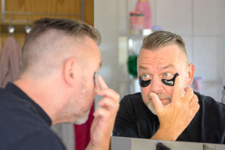 Man applying a cosmetic gel hydration patch to the skin below his eye in a skin care treatment...