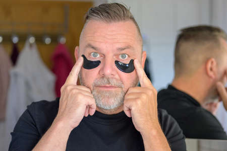 Man using gel patches to hydrate the skin under his eyes in a skincare and cosmetology concept