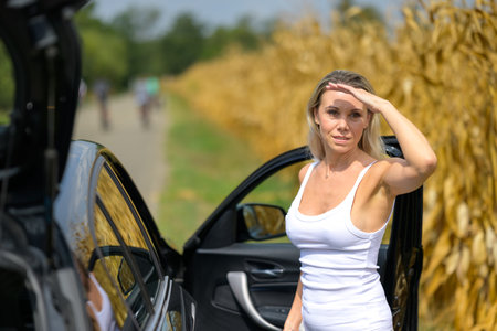 Woman standing by a car with a thoughtful look because of an car failure waiting for help with her to hand to the foreheadの写真素材