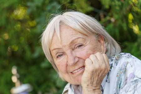 Attractive senior grandmother with a happy friendly smile in a close up portrait in a lush garden
