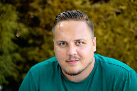 Young man looking intently at the camera with a quiet thoughtful smile outdoors in fallの写真素材
