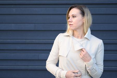 Attractive middle-aged blond woman looking thoughtful to the side in front of a blue wall