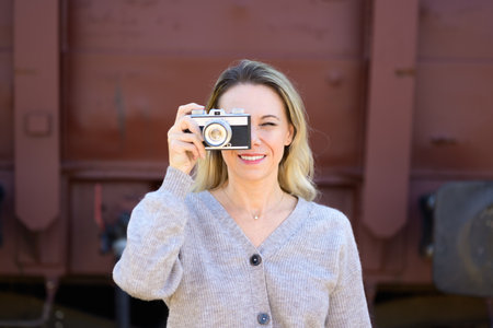 Smiling middle aged woman with an old camera is taking a picture and looking through the viewfinder