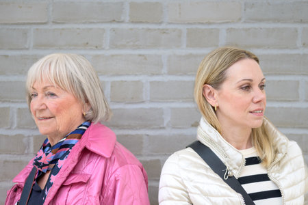 Close up of mother and daughter standing in front of a white wall while looking in opposite directionの写真素材