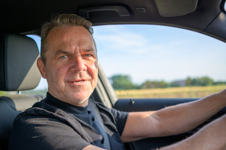 Middle aged man driving in his car and looking to cameraの写真素材
