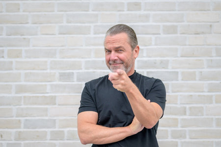Portrait of an attractive serious man pointing to camera in front of a white brick wallの写真素材