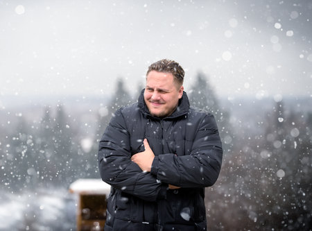 Young man in a thick winter jacket looking critically to the side, outdoor in Winterの写真素材