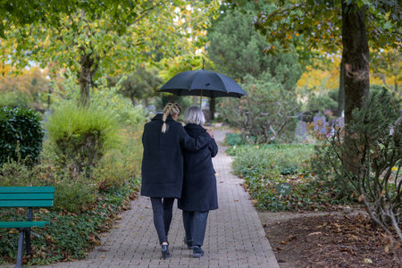 Rear view of daughter holding her mother in her arms on the way to the man's grave in the cemetery...