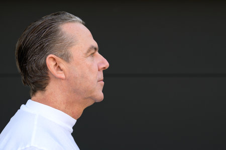Side view portrait of a middle aged man with his mouth closed in front of a black wall