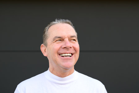 A middle aged man in a white turtle neck t shirt giving a very big smile and looking to sideの写真素材