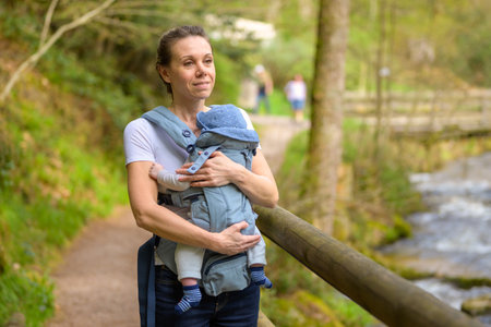 Happy woman looking to distance while holding and carrying it in a baby carrier in a parkの写真素材